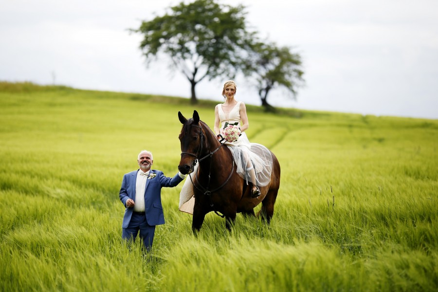 Manželská fotografie na louce, manželka oblečená v bílých šatech jede na koni z naši stáje JS Vydlákov